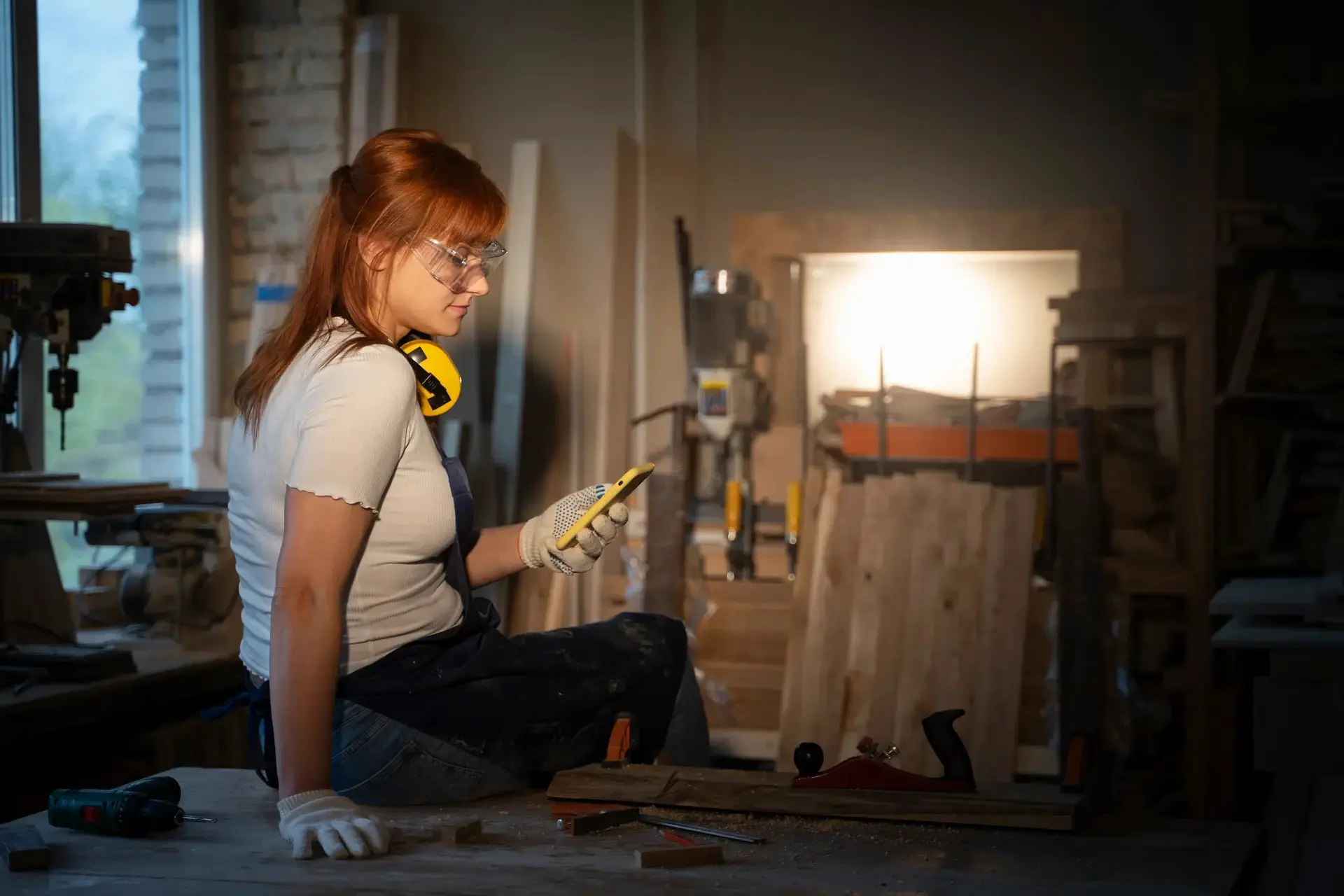 Woman in safety glasses viewing a mobile phone in a craft workshop